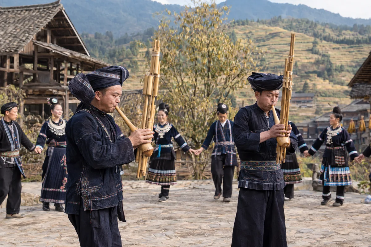 Two lusheng players with village dancers behind them